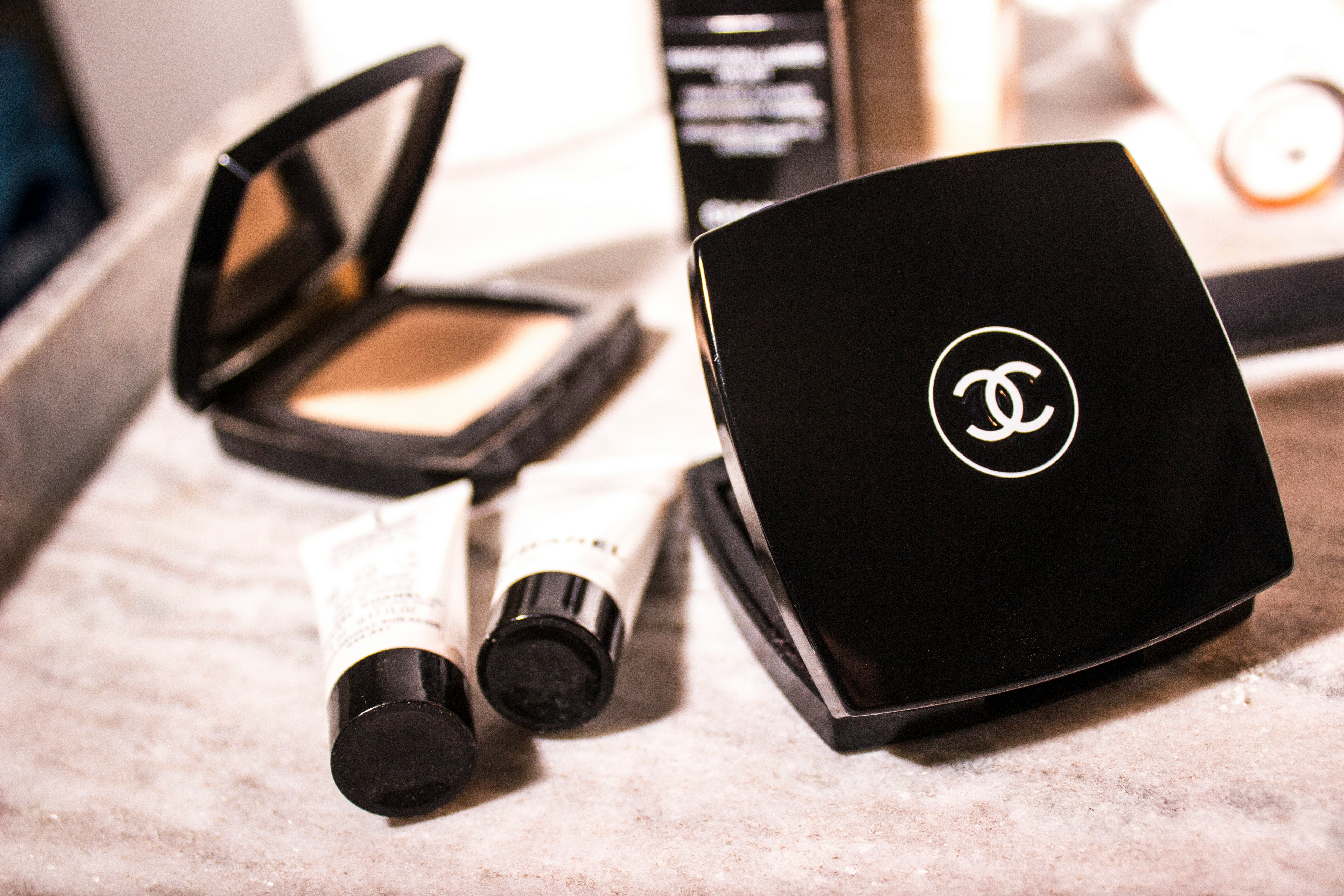 Two compacts of beige powder and two small tubes on a marbled counter