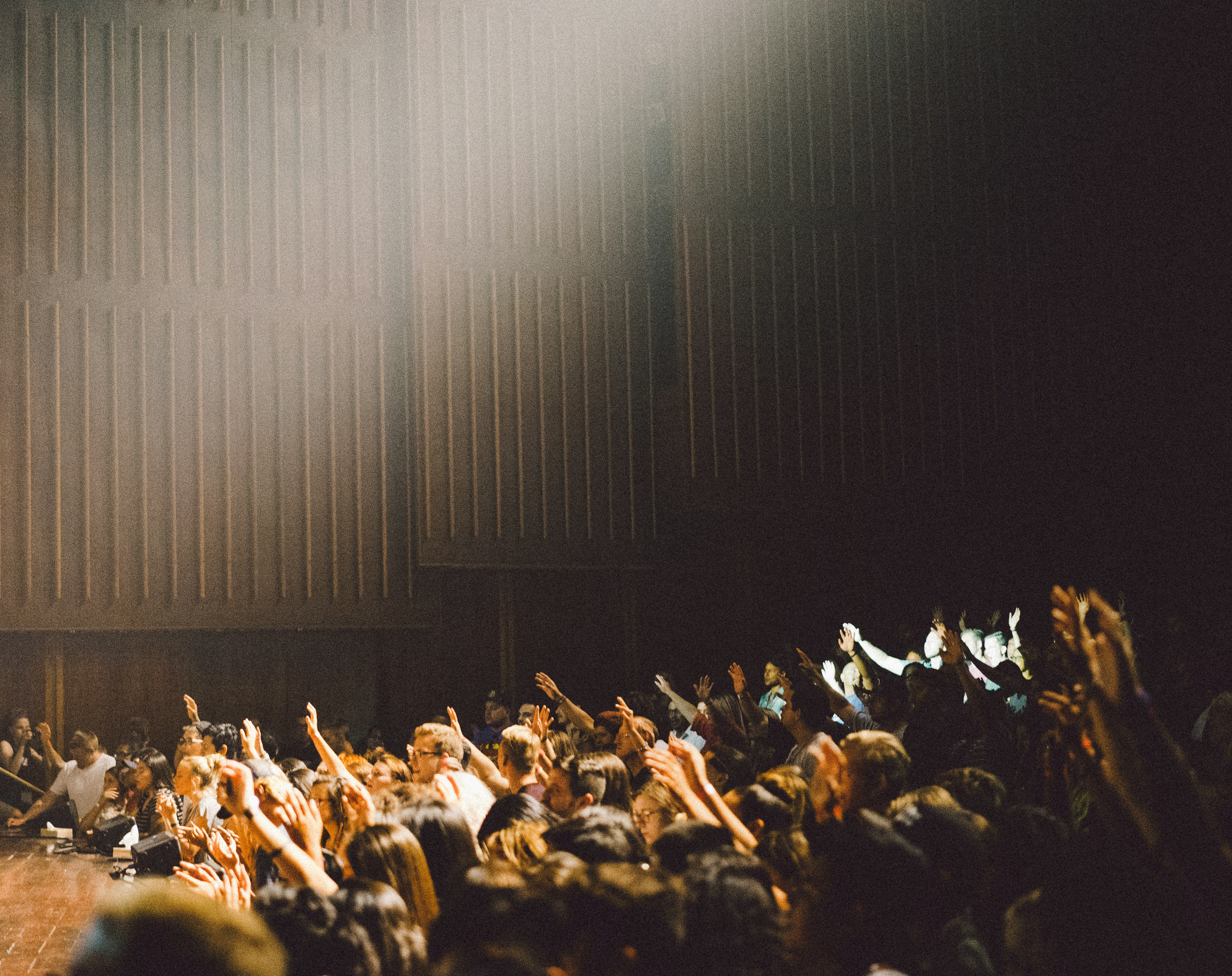 A wide lecture hall with students all raising their hands