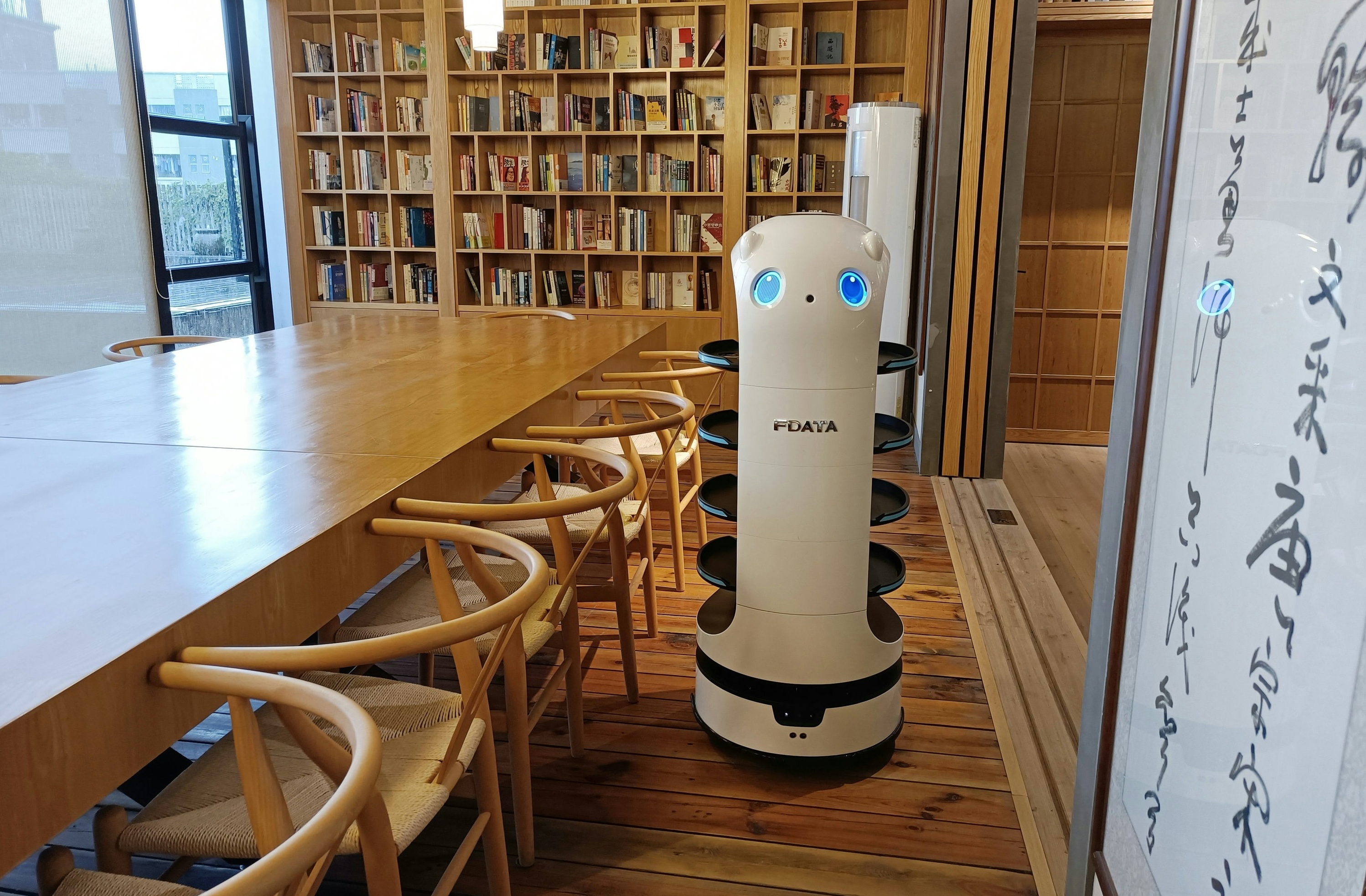 A tall robot with wheels next to a cleared library table and chairs