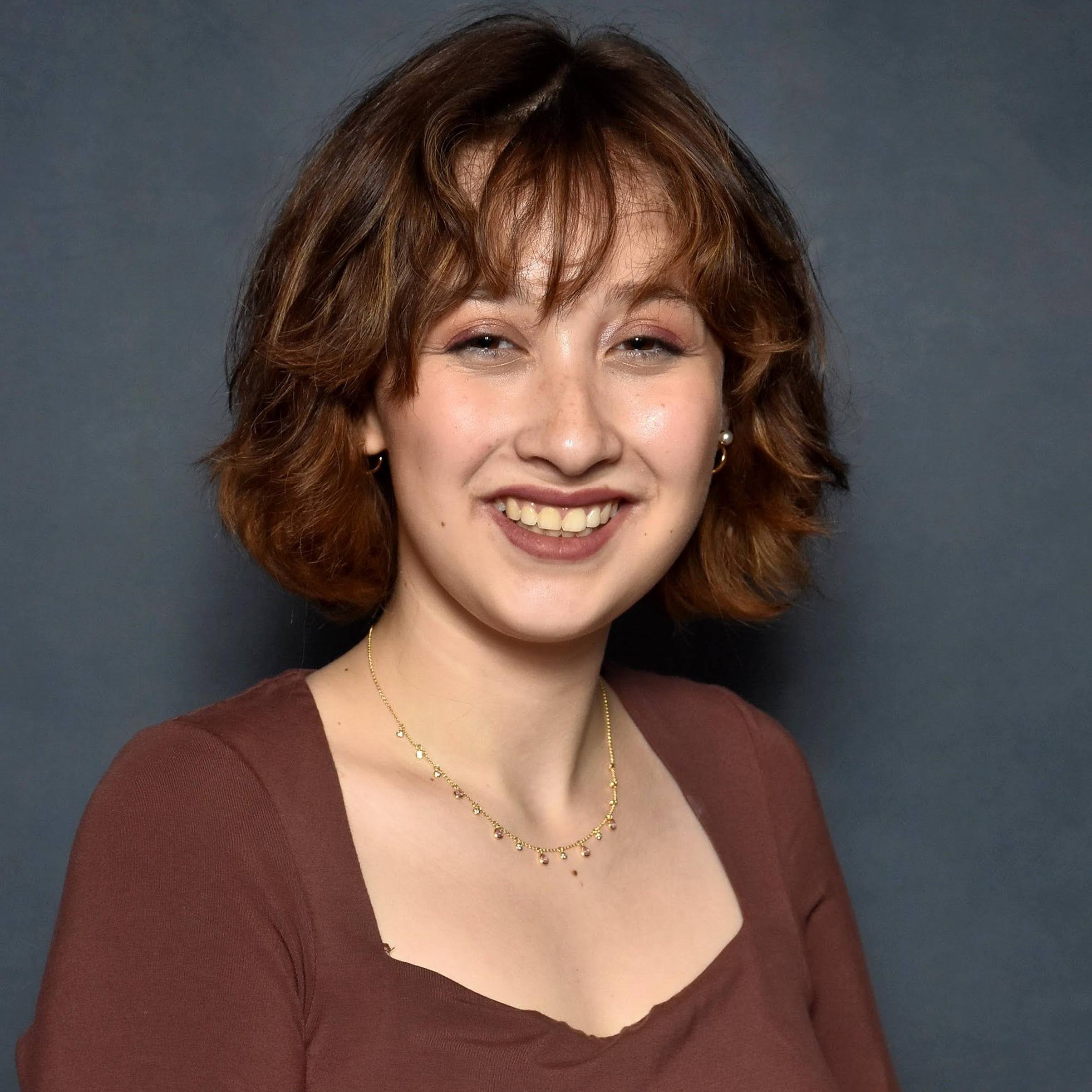 A photo of Abby Carr grinning in a brown top
